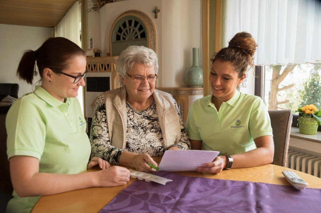 Kristina und Isabell beraten eine Seniorin zu Hause zum Pflegegrad-Antrag